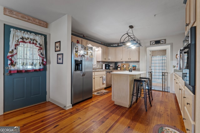 kitchen with hardwood / wood-style flooring, appliances with stainless steel finishes, tasteful backsplash, hanging light fixtures, and a center island