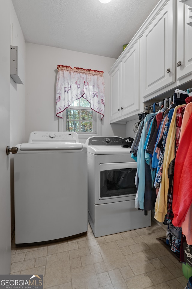 washroom featuring washing machine and dryer, cabinets, and a textured ceiling