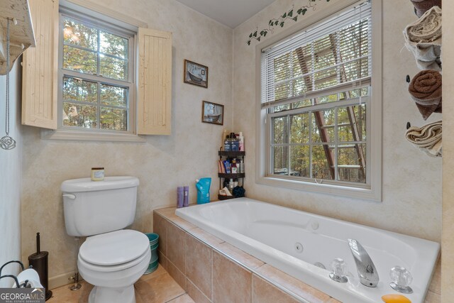 bathroom featuring tile patterned floors, a healthy amount of sunlight, toilet, and a relaxing tiled tub