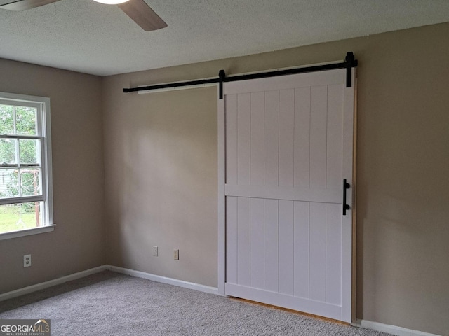 unfurnished bedroom with a barn door, carpet floors, multiple windows, and ceiling fan