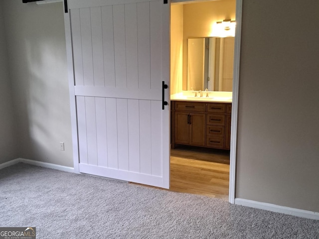 unfurnished bedroom with ensuite bathroom, a barn door, light colored carpet, and sink