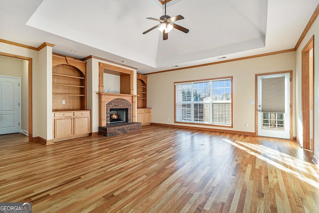 unfurnished living room with a raised ceiling, a brick fireplace, ceiling fan, and light wood-type flooring