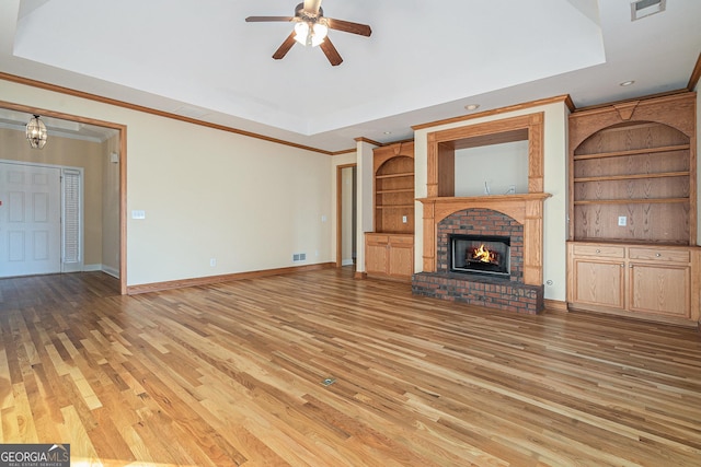 unfurnished living room with a raised ceiling, ceiling fan, light wood-type flooring, a fireplace, and ornamental molding