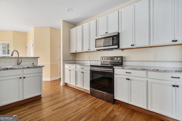 kitchen featuring white cabinets, sink, light stone countertops, appliances with stainless steel finishes, and light hardwood / wood-style floors