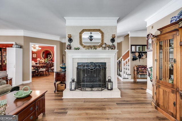 living room with ornamental molding, a fireplace, light hardwood / wood-style floors, and ceiling fan with notable chandelier