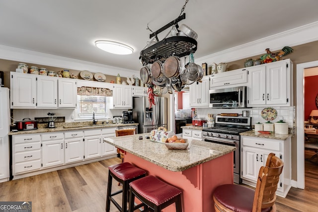 kitchen with stainless steel appliances, white cabinets, a kitchen island, and ornamental molding