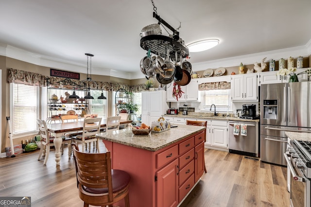 kitchen featuring ornamental molding, white cabinetry, appliances with stainless steel finishes, light hardwood / wood-style floors, and a center island