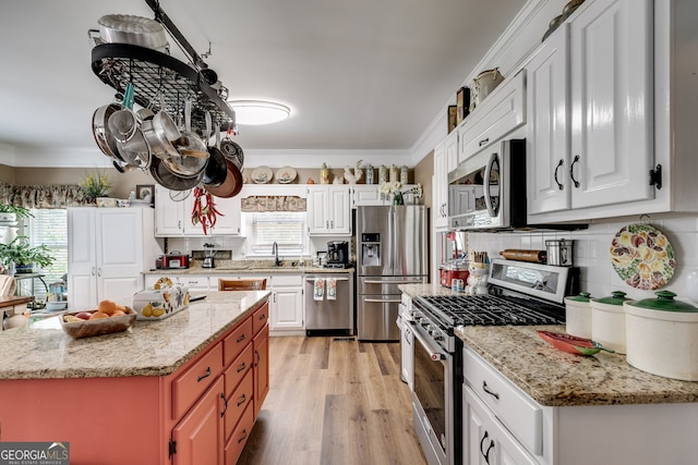 kitchen featuring white cabinetry, appliances with stainless steel finishes, ornamental molding, a center island, and light wood-type flooring