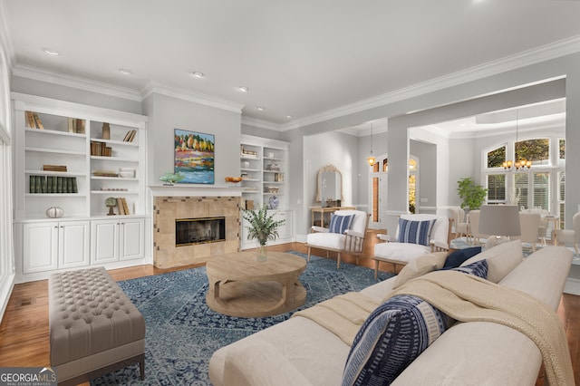 living room featuring a tile fireplace, ornamental molding, wood-type flooring, and a notable chandelier