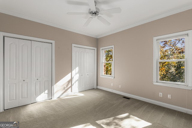 unfurnished bedroom featuring ceiling fan, ornamental molding, light carpet, and two closets