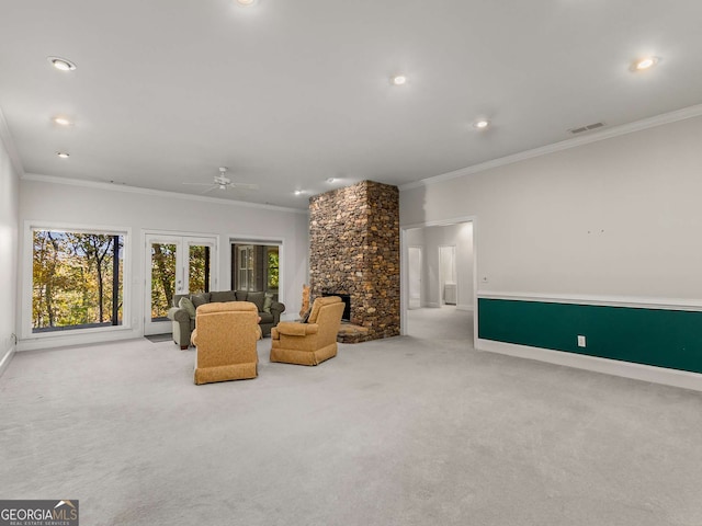 carpeted living room with a stone fireplace, crown molding, and ceiling fan