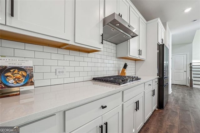 kitchen with dark wood-type flooring, tasteful backsplash, light stone countertops, white cabinetry, and appliances with stainless steel finishes