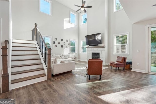 living room with ceiling fan, a high ceiling, a stone fireplace, and dark hardwood / wood-style flooring