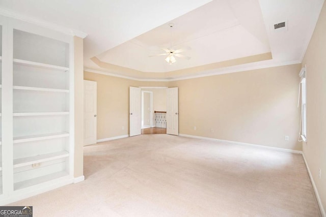 carpeted spare room featuring built in shelves, ceiling fan, crown molding, and a tray ceiling