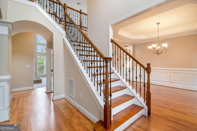 staircase featuring hardwood / wood-style floors, a chandelier, ornamental molding, and a tray ceiling