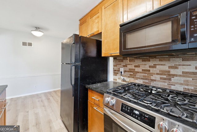 kitchen featuring dark stone countertops, backsplash, light wood-type flooring, and black appliances