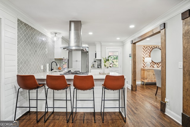 kitchen with a kitchen breakfast bar, dark hardwood / wood-style floors, island range hood, white cabinets, and ornamental molding