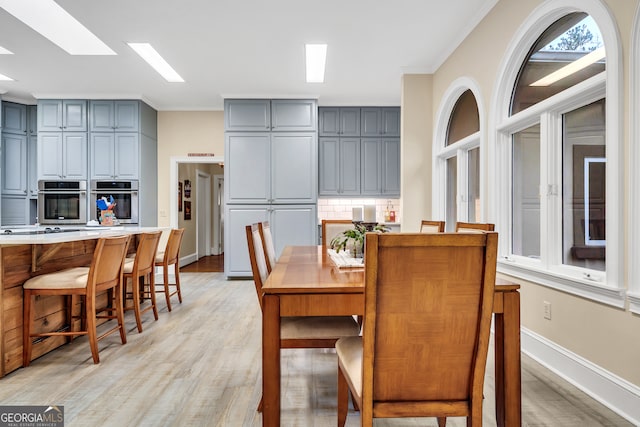 dining space with a skylight, ornamental molding, and light wood-type flooring