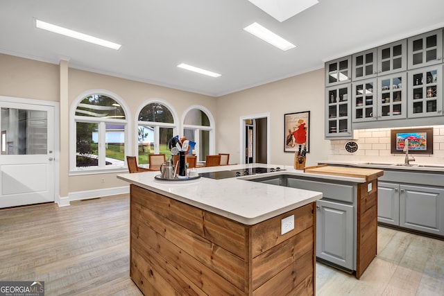 kitchen with ornamental molding, gray cabinets, a center island, backsplash, and light wood-type flooring