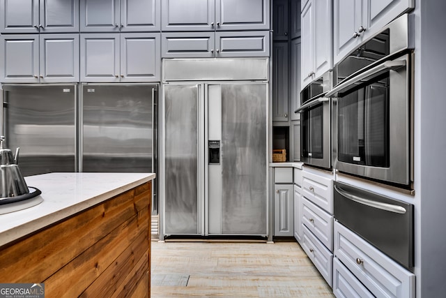 kitchen featuring gray cabinetry, light wood-type flooring, stainless steel appliances, and light stone counters