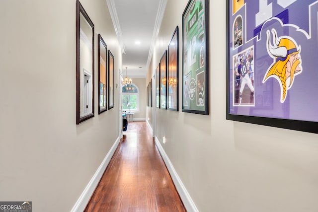 hall featuring crown molding, wood-type flooring, and an inviting chandelier