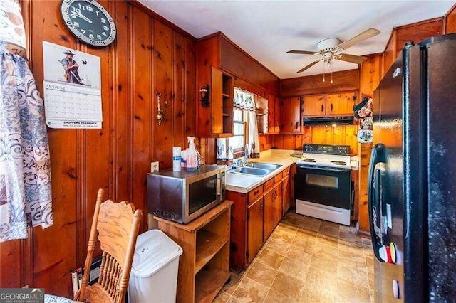 kitchen featuring ceiling fan, sink, white electric range oven, wood walls, and black refrigerator