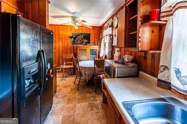 kitchen featuring black fridge with ice dispenser, wooden walls, ceiling fan, and sink