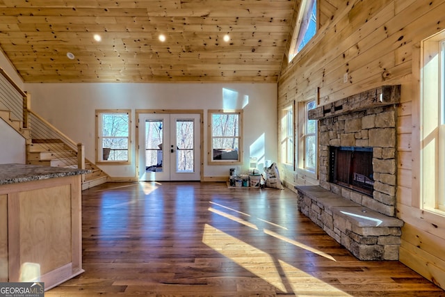 unfurnished living room featuring french doors, high vaulted ceiling, dark hardwood / wood-style floors, and a stone fireplace