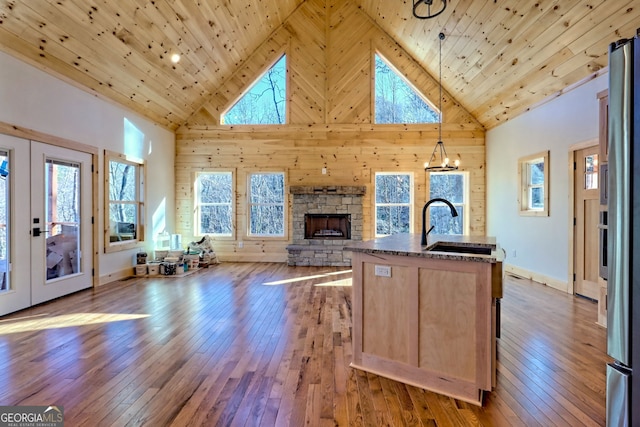 kitchen featuring sink, a stone fireplace, hanging light fixtures, wood ceiling, and a kitchen island with sink