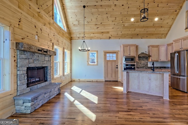 kitchen with a fireplace, hanging light fixtures, stone counters, appliances with stainless steel finishes, and light brown cabinetry