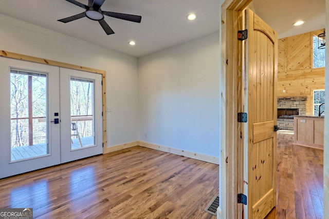 entryway featuring hardwood / wood-style floors, french doors, ceiling fan, and a stone fireplace