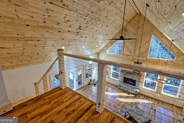 unfurnished living room with hardwood / wood-style floors, wood walls, a stone fireplace, wooden ceiling, and high vaulted ceiling