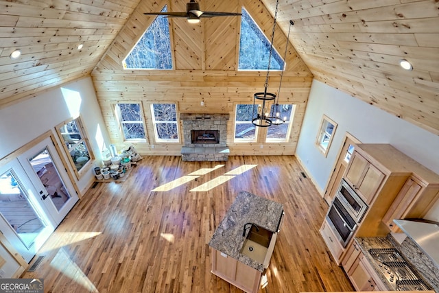 unfurnished living room featuring high vaulted ceiling, wooden ceiling, a stone fireplace, and light hardwood / wood-style flooring