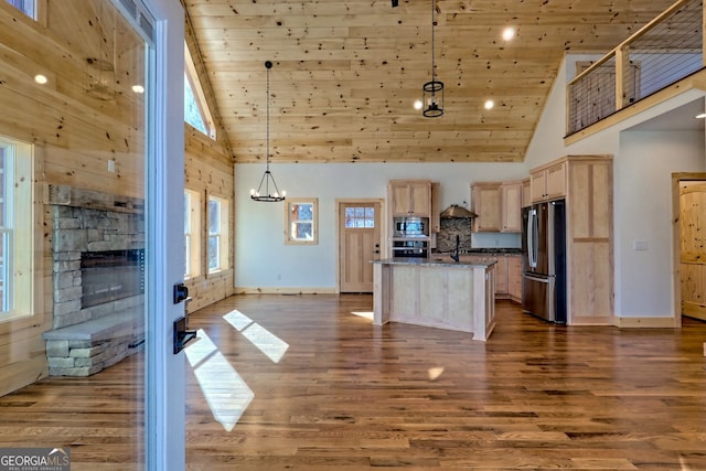 kitchen with a center island with sink, light stone countertops, appliances with stainless steel finishes, light brown cabinets, and pendant lighting