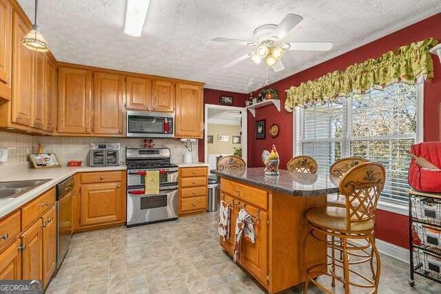 kitchen with a kitchen bar, stainless steel appliances, ceiling fan, pendant lighting, and a center island