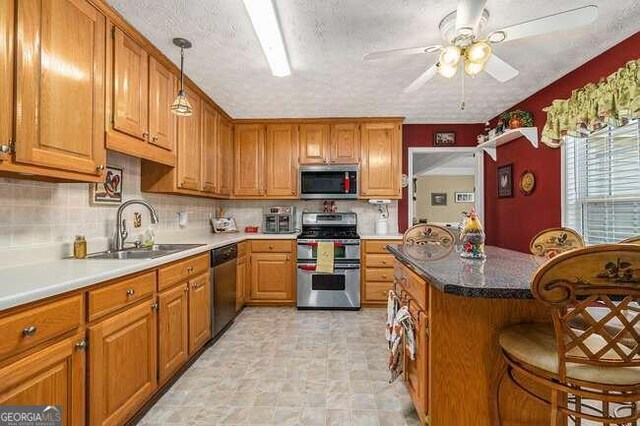 kitchen with ceiling fan, sink, hanging light fixtures, stainless steel appliances, and a kitchen breakfast bar