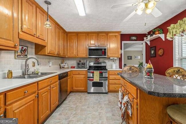 kitchen featuring ceiling fan, sink, a kitchen breakfast bar, decorative light fixtures, and appliances with stainless steel finishes