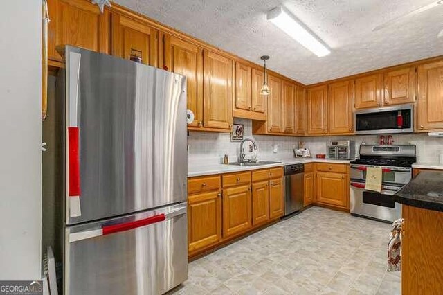 kitchen with backsplash, hanging light fixtures, sink, a textured ceiling, and appliances with stainless steel finishes