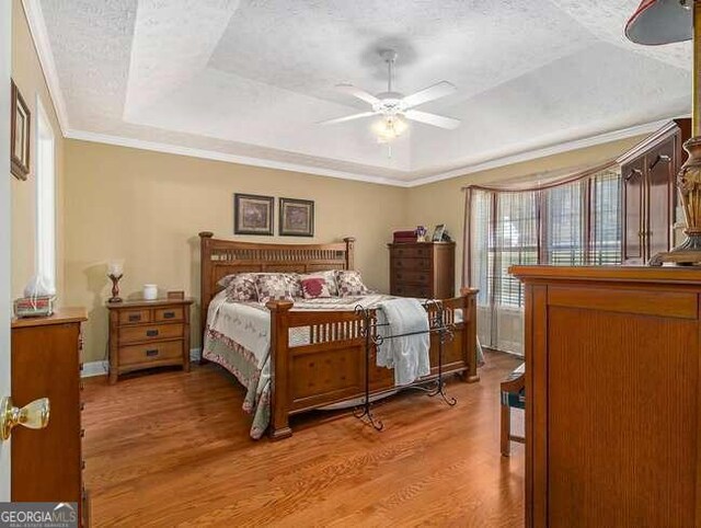 bedroom with ceiling fan, a raised ceiling, hardwood / wood-style floors, a textured ceiling, and ornamental molding