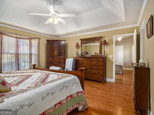 bedroom with crown molding, ceiling fan, light wood-type flooring, a textured ceiling, and a tray ceiling