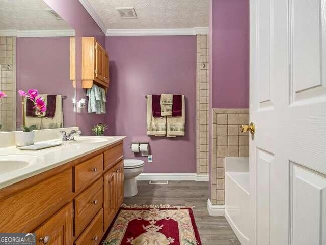 bathroom featuring a bathtub, vanity, ornamental molding, a textured ceiling, and wood-type flooring