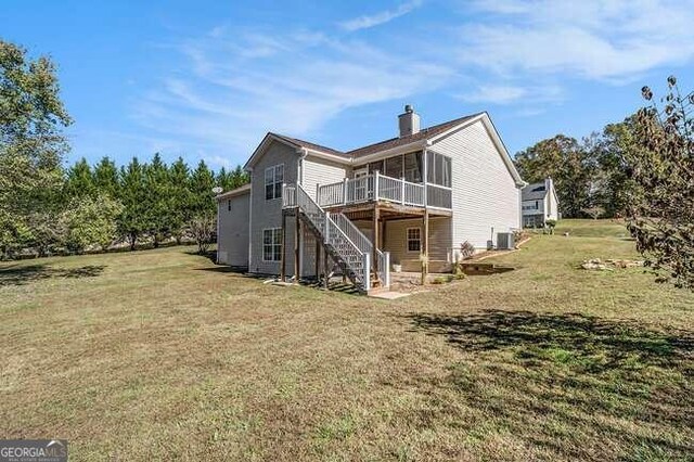 rear view of house with a lawn, a sunroom, a deck, and central AC