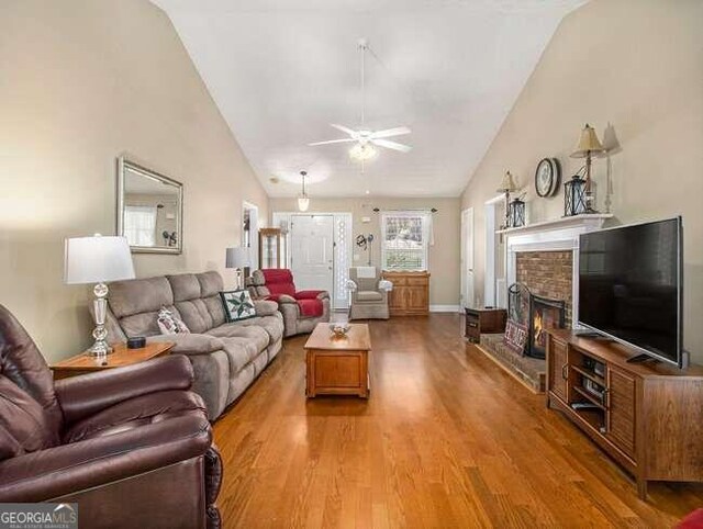 living room featuring hardwood / wood-style flooring, ceiling fan, lofted ceiling, and a fireplace