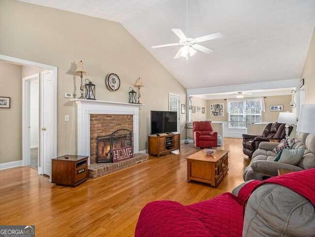 living room featuring ceiling fan, light wood-type flooring, a fireplace, and high vaulted ceiling