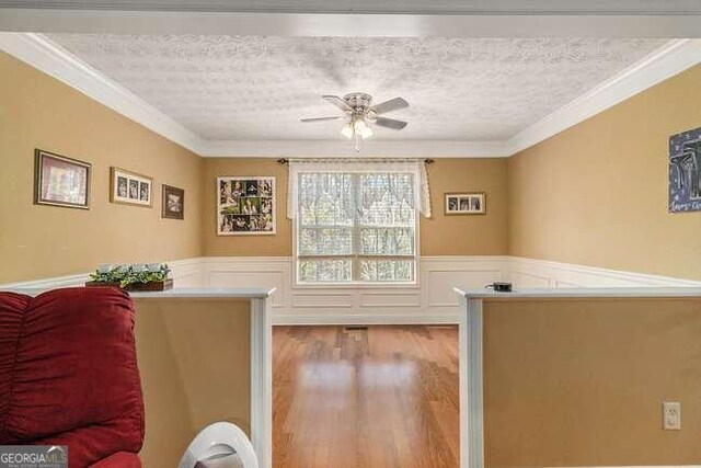 living room featuring ceiling fan, light hardwood / wood-style flooring, a textured ceiling, and ornamental molding