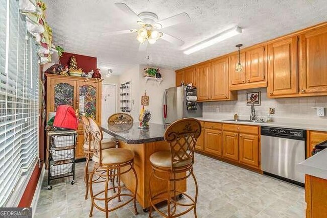 kitchen with a kitchen bar, a textured ceiling, stainless steel appliances, sink, and pendant lighting