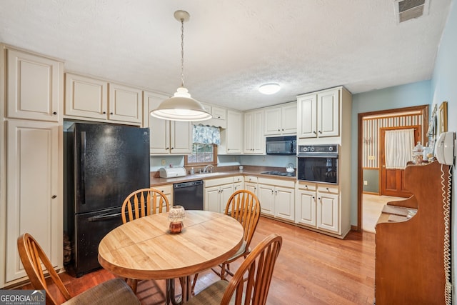 kitchen with sink, light hardwood / wood-style floors, a textured ceiling, decorative light fixtures, and black appliances