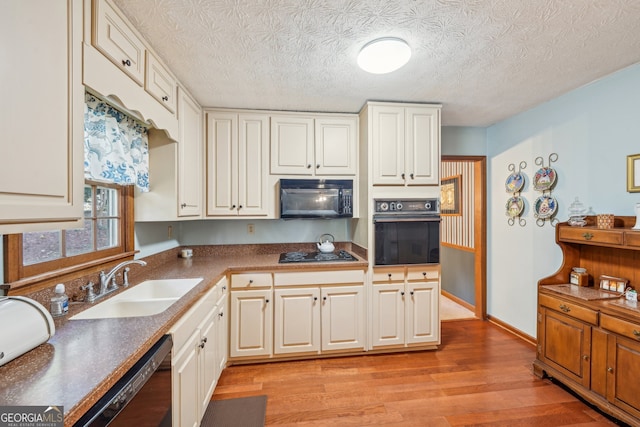 kitchen featuring light wood-type flooring, a textured ceiling, sink, black appliances, and white cabinetry