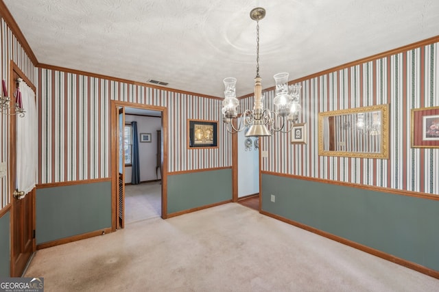 carpeted empty room featuring a chandelier, a textured ceiling, and ornamental molding