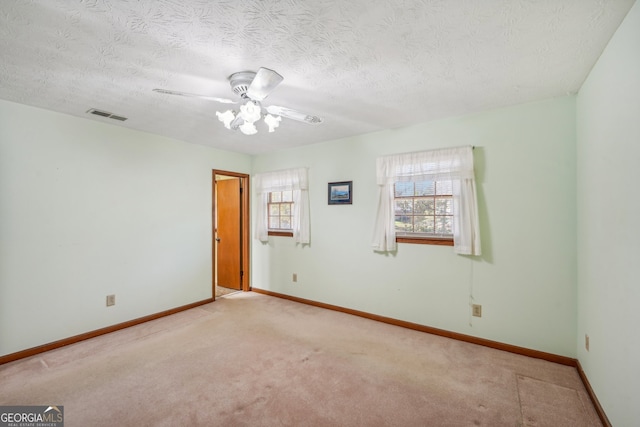 empty room featuring a textured ceiling, light colored carpet, and ceiling fan